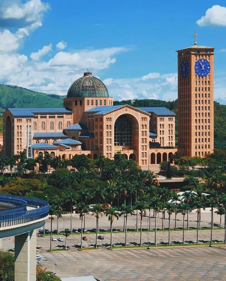 A basílica de Aparecida, de tijolos, com cúpula e torre alta, vista de longe.