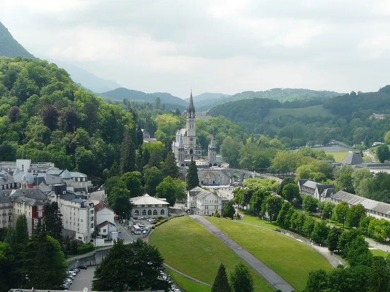 Vale de Lourdes visto do alto, com a esplanada verde e a basílica ao fundo, entre montanhas.