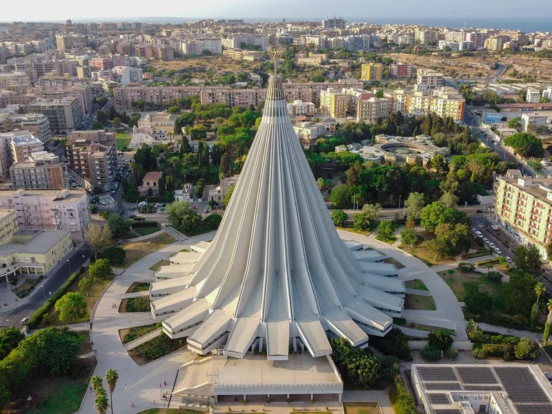 Vista aérea do santuário de Siracusa, uma grande cobertura cônica de concreto entre os prédios da cidade.