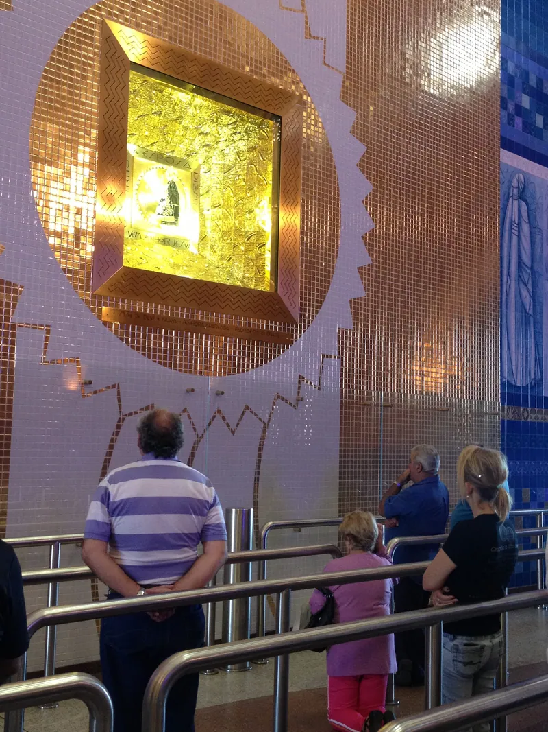 Devotos rezam diante do nicho dourado onde fica a pequena imagem escura de Nossa Senhora Aparecida.