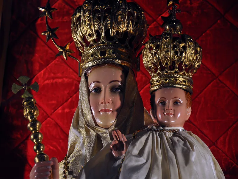 Imagem de Maria com o Menino, ambos com coroas douradas altas, diante de um fundo vermelho.