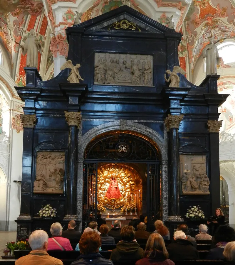 A capela da graça, de mármore negro, dentro da igreja da abadia; ao centro, a pequena imagem escura de Maria, e fiéis sentados à frente.