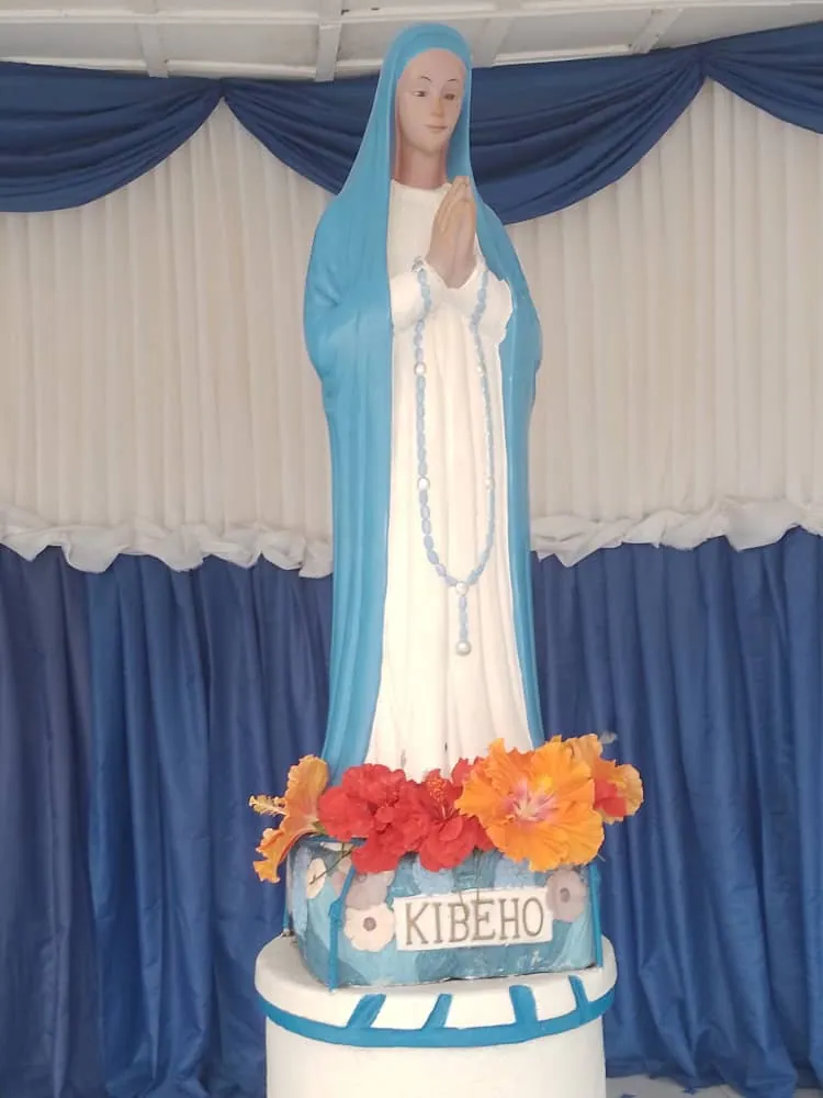 Estátua de Maria com manto azul e veste branca, de mãos postas, sobre um pedestal com a inscrição «Kibeho».
