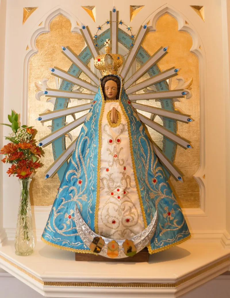 Pequena imagem de Maria em manto azul e branco com raios dourados ao redor, num pedestal.